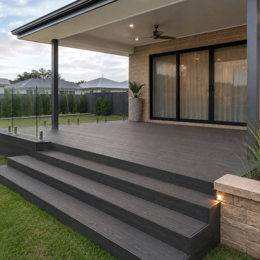 Modern outdoor deck and staircase system in black composite lumber, attached to a house with brick walls and large sliding glass doors.